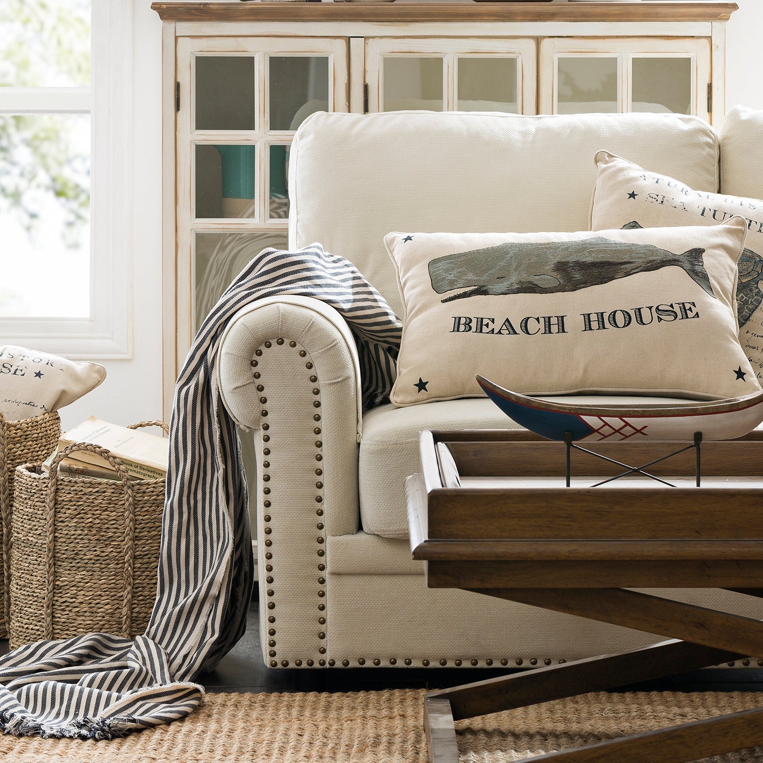 Beige tufted sofa with nautical-themed cushions, complemented by a rustic wooden coffee table, creating a cozy beach house vibe. Explore sofas and couches collection at Loft Home.