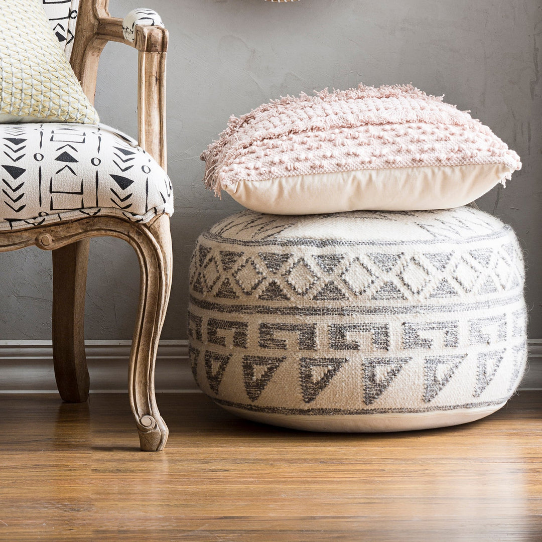 Boho-style ottoman with geometric patterns, topped with a textured cushion, paired with a vintage chair, adding comfort and charm to the space.