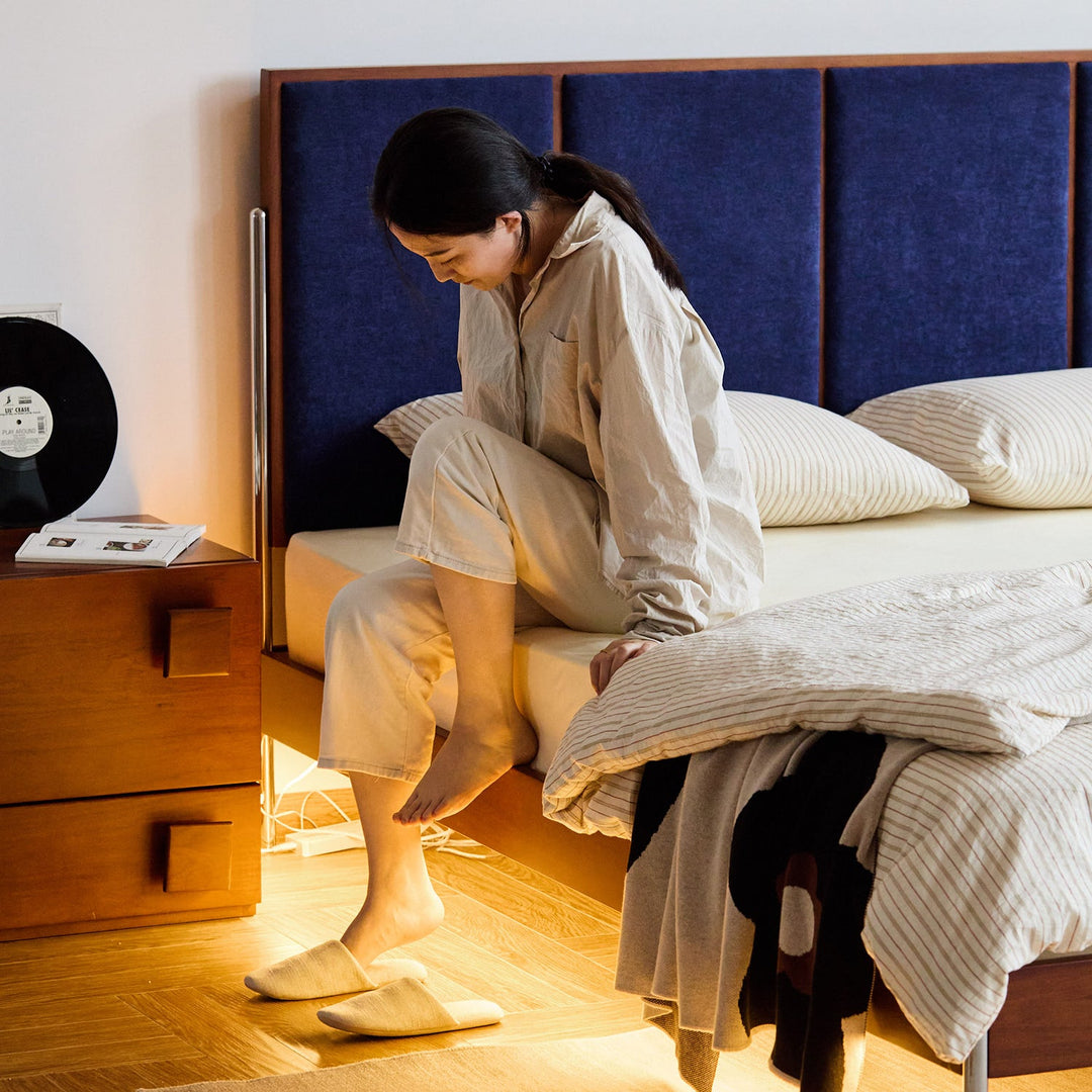 Modern wooden bed frame with navy upholstered headboard, styled with striped bedding and warm under-bed lighting, ready in stock for fast delivery.