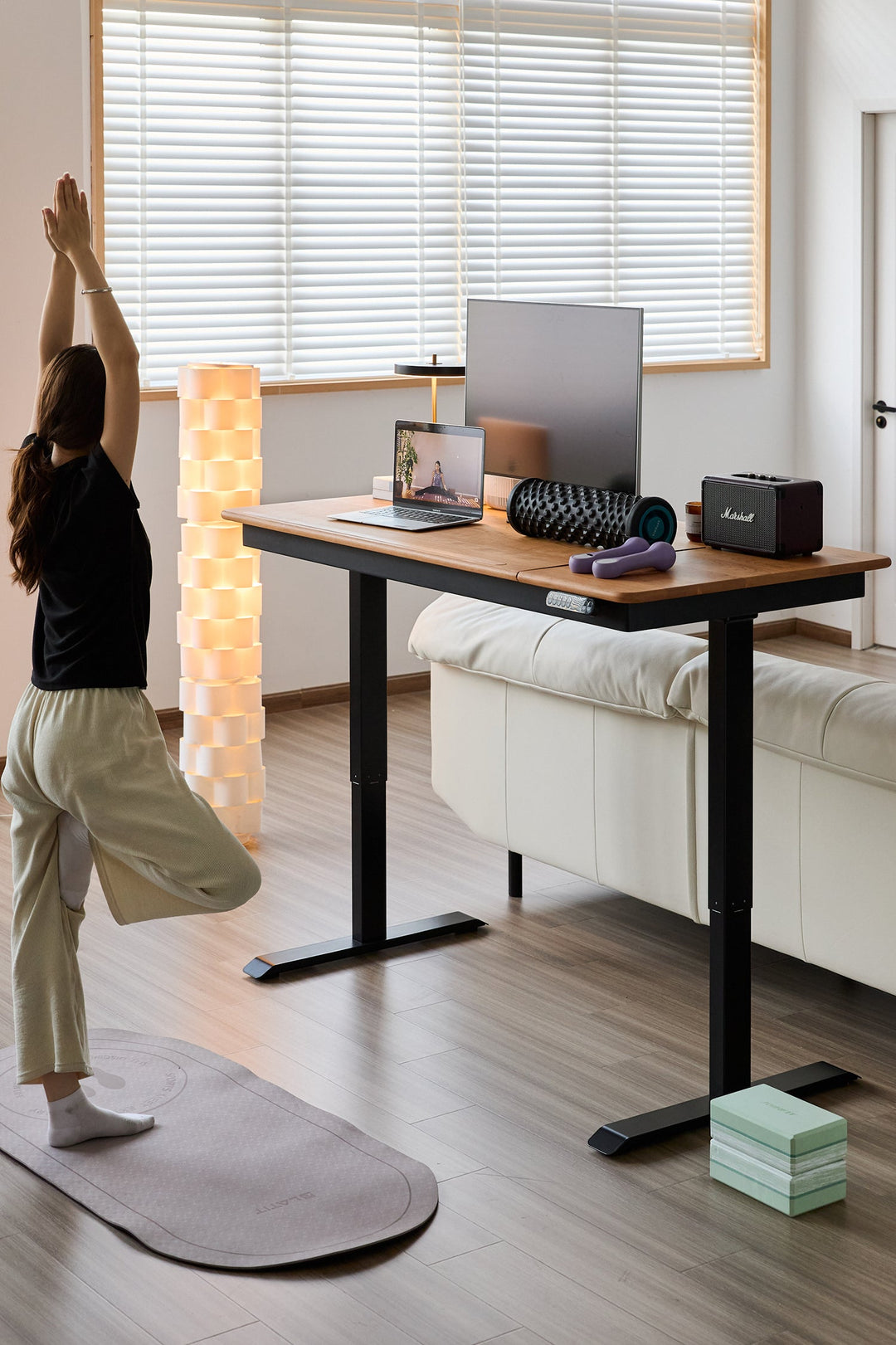 Person stretching in a home office with a standing desk and yoga mat.